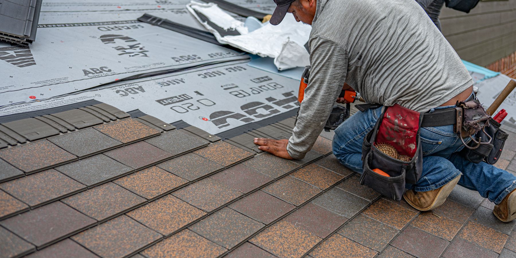 Roofer laying asphalt shingles over underlayment on a Long Island roof